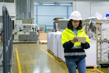 Focused female engineer with tablet computer monitoring equipment onsite. Middle aged woman in...