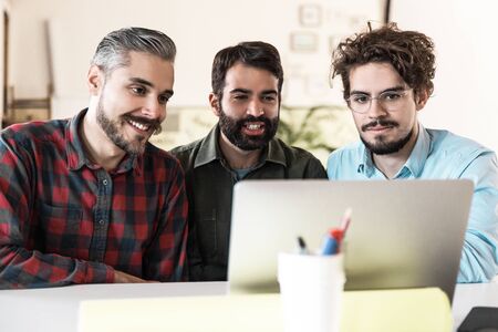 Happy startup team watching presentation on monitor, using laptop for video call. Business...