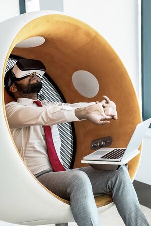 Businessman in VR headset stretching hands. Young African American businessman using virtual reality...
