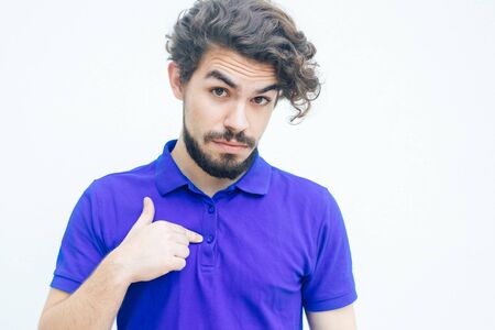 Surprised guy pointing finger at himself with questioning face. Handsome bearded young man in blue...