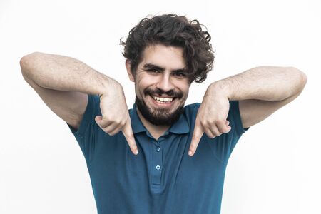 Joyful positive guy pointing fingers down at copy space. Handsome bearded young man in blue casual...