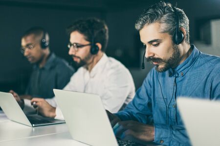 Handsome young man with headset typing on laptop. Confident client support team at workplace. Call...
