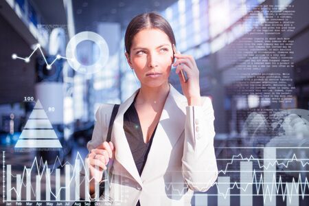 Concentrated young businesswoman talking on phone in office corridor with virtual business chars....