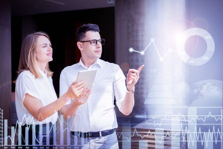 Confident businessman pointing at virtual business diagrams. Young Caucasian man wearing glasses...