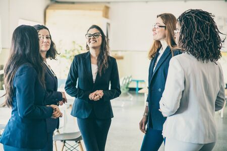 Group of smiling female workers talking in open space office. Cheerful young women standing in...