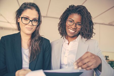 Smiling African American woman turning page of document. Front view of professional business team holding paper instructions and looking at camera. Business conceptの写真素材