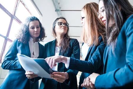 Group of focused women studying new project. Low angle shot of concentrated business team reading document. Teamwork conceptの写真素材
