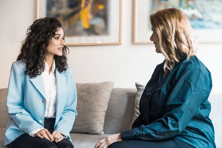 Smiling businesswomen talking while sitting on sofa. Cheerful confident women sitting on sofa and communicating. Communication conceptの写真素材
