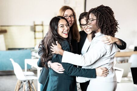 Successful female business team hugging in office. Group of smiling young woman embracing in circle. Teamwork conceptの写真素材
