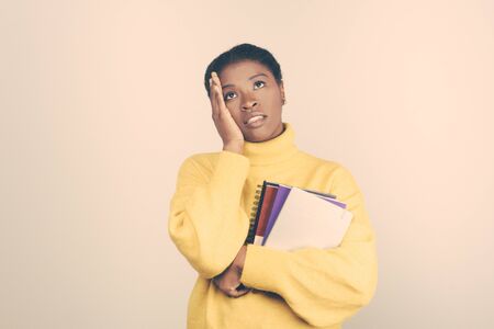 Worried young student holding hand on head and looking up. Disquieting young lady holding notepads. Education, tuition conceptの写真素材