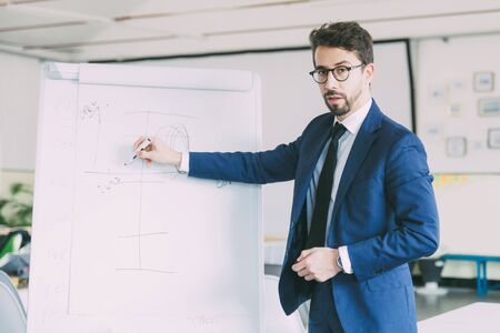 Business coach standing near whiteboard and looking at camera. Confident Caucasian manager doing presentation. Business training conceptの写真素材