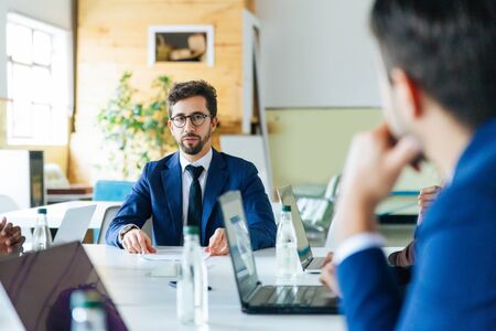 Focused project manager looking at worker. Employees sitting at table during morning briefing. Business meeting conceptの写真素材