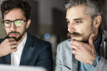 Two thoughtful businessmen looking at laptop. Confused business partners thinking and looking at laptop. Business, working late conceptの写真素材