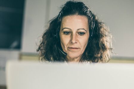 Tilted view of call center operator. Front view of focused mature woman talking with interlocutor....