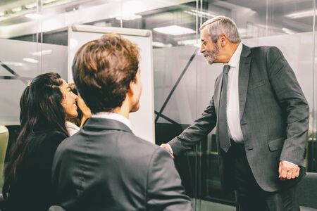 Smiling business leader shaking hands with subordinates. Cheerful office workers greeting each other. Business meeting conceptの写真素材