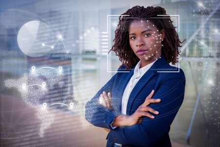 Woman posing near building and virtual identification graphics. Young African American businesswoman with arms crossed standing outside, looking at camera. Confident businesswoman conceptの写真素材