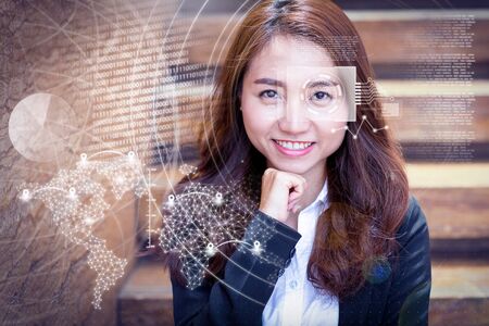 Smiling young Asian woman and virtual identification graphics. Closeup portrait of pretty businesswoman looking at camera and leaning on hand with stairs in background. Front view.の写真素材