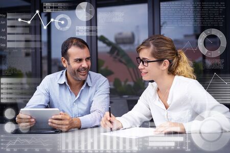 Colleagues talking in office and virtual statistic graphics. Portrait of male and female communicating. Young Caucasian businesswoman and mid adult bearded man with digital tablet. Corporate conceptの写真素材