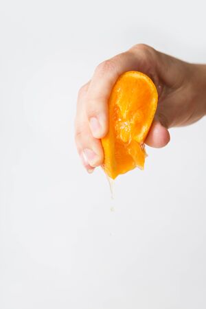 Hand of woman squeezing orange for juice isolated on white background. Cropped shot, closeup. Fresh juice or organic food conceptの写真素材