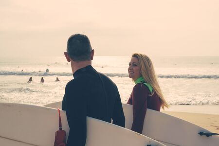 Couple holding surfboards and walking on beach. Cheerful man and woman in wetsuits holding...