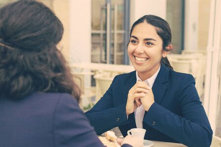 Smiling businesswomen talking and drinking coffee. Professional female coworkers in formal wear sitting at table and drinking coffee together in outdoor cafe. Coffee time concept