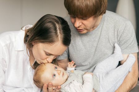 Happy new parents holding and kissing cute baby daughter. Young couple holding six month child and...