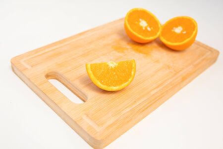 Quarter of orange in focus and two halves of orange out-of-focus laying on wooden board isolated on white background. Close-up side view. Citrus fruit and healthy food conceptの写真素材