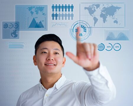 Dreamy young Asian man using virtual statistics and touching transparent screen with finger. Coach using touch sensitive glass board. Business and presentation conceptの写真素材
