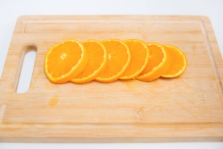 Thin sliced orange circles laying on wooden board. Isolated on white background. Close-up side view....