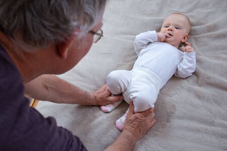 Grey haired grandfather enjoying leisure time with baby granddaughter, holding her legs in play....
