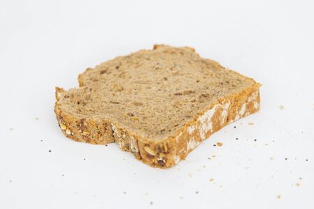 Sliced piece of rye bread with cereals. Crumbs laying around. Natural brown loaf slice isolated on...