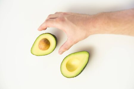 Person taking cut half of avocado with core for cooking. Top view. Isolated object on white...