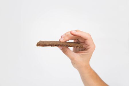 Hand holding slice of black rye unleavened bread. Isolated object on white background. Healthy diet or organic food conceptの写真素材