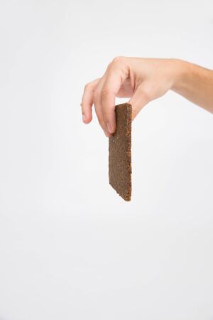 Female hand holding thin slice of black rye bread. Isolated object on white background. Healthy diet or organic food conceptの写真素材