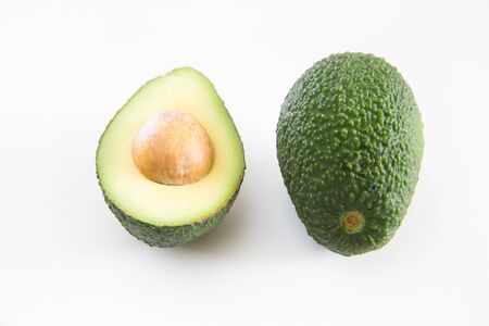 Half of avocado with seed and whole fruit. Closeup shot. Isolated object on white background. Fresh food or healthy diet conceptの写真素材