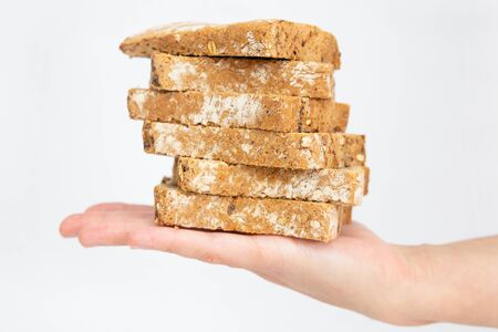 Stack of brown bread slices laying on female palm. Homemade cereal loaf pieces isolated on white background. Studio shot. Side view. Cooking and baking at home conceptの写真素材