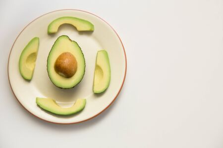 Parts of avocado on ceramic plate, half with core and cut slices. Top view, copy space. Isolated...