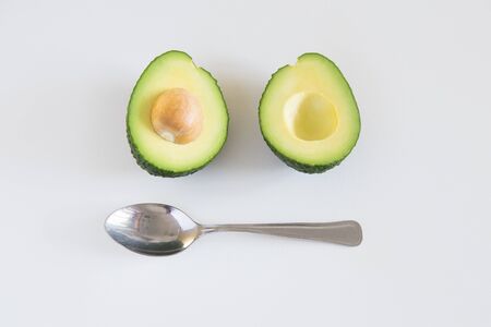 Metal spoon and halved avocado with seed. Top view. Isolated objects on white background. Fresh food...