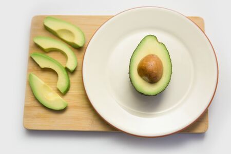 Avocado half on plate and fruit slices on wooden chopping board. Top view. Isolated objects on white background. Fresh food or healthy diet conceptの写真素材