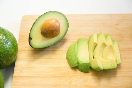 Sliced avocado and halved fruit with seed on chopping board. Top view. Isolated objects on white background. Fresh food or healthy diet conceptの写真素材