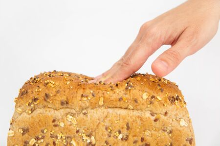 Cropped view of hand pushing soft brick form bread with fingers. Fresh loaf with cereals, oats,...