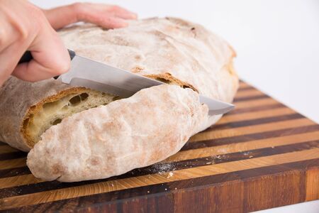 Person cutting crusty piece of freshly baked bread on chopping board. Isolated object on white...