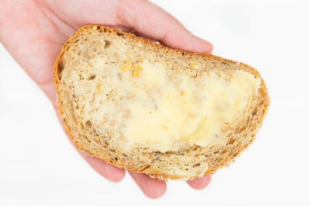 Hand holding slice of wholegrain loaf with dairy butter isolated over white background. Closeup shot, top view. Traditional bread or breakfast conceptの写真素材