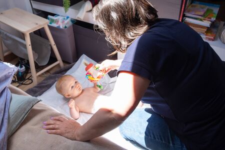 Babysitter soothing baby lying in beddings, playing with child with rattle toy. Staying at home and child care conceptの写真素材