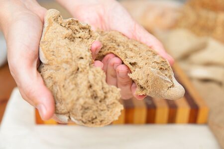 Human hands tearing freshly baked whole grain bun for eating. Closeup shot. Traditional bread or...