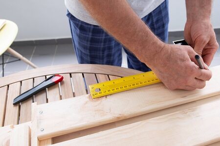 Craftsman marking wooden part with pencil and construction ruler. Senior man working at balcony. Closeup view. House improving and home decoration during quarantine conceptの写真素材
