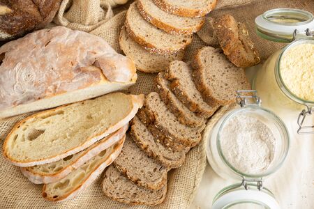 Freshly baked traditional wheat and whole grain baguettes cut in slices, burlap sackcloth and flour...