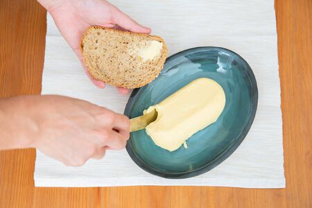 Hands of woman with toast and knife cutting butter on table with napkin. Closeup shot, top view. Traditional bread or breakfast conceptの写真素材