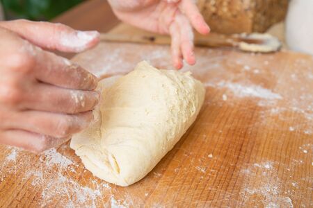 Kneaded dough for pastry on wooden board. Baker hand in flour preparing bread. Selective focus....