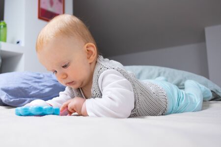 Focused cute red haired baby playing with rattle, studying toy while lying on belly on parents bed. Closeup shot. Childhood or staying at home conceptの写真素材